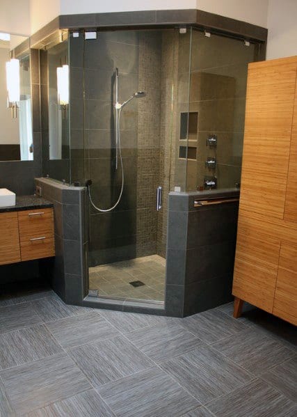 Modern corner bathroom with glass shower enclosure, wooden cabinets, and gray tiled floor