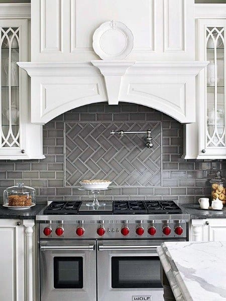 White kitchen with gray herringbone backsplash, stainless steel stove, and decorative cabinetry