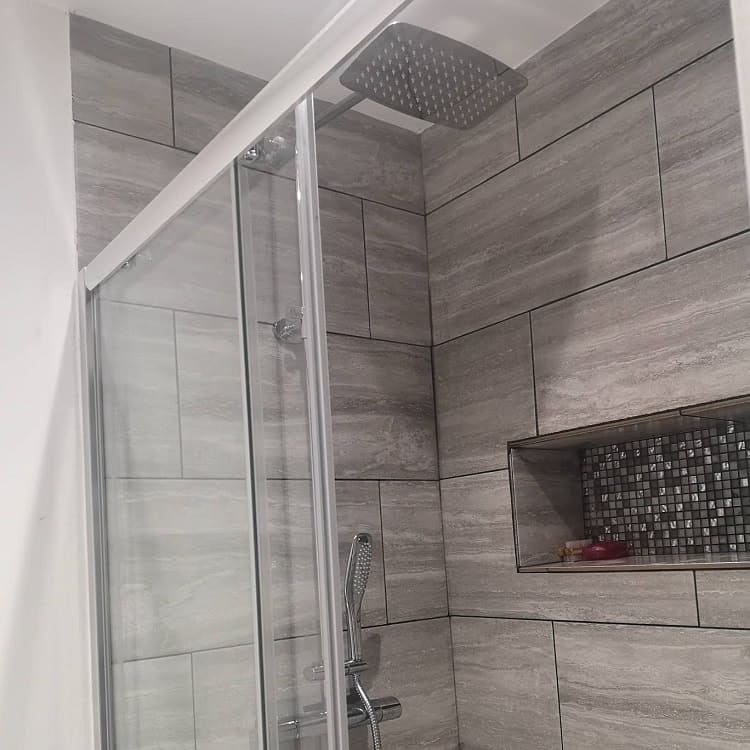 Modern shower with grey tiles, glass door, and recessed shelf with mosaic tiles.