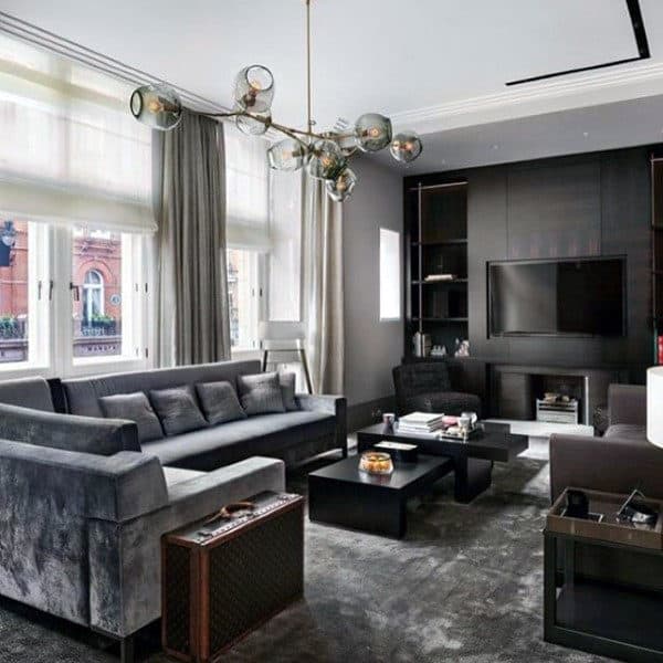 Grey tones living room with velvet sofa, modern chandelier, and sleek entertainment center.