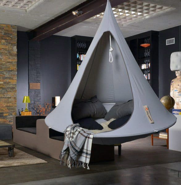 Hanging cocoon-style hammock in a modern living room with cozy pillows and industrial decor.