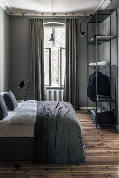 Minimalist bedroom with a bed, grey bedding, a tall open wardrobe, and a window with long curtains