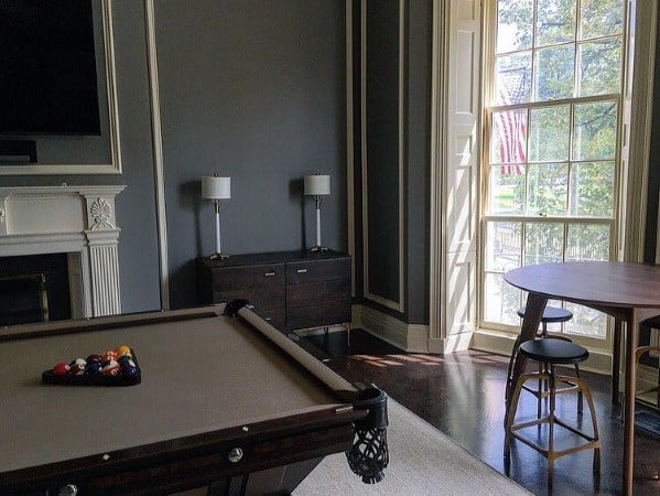 Modern billiard room with gray walls, white fireplace, and large windows for natural light.