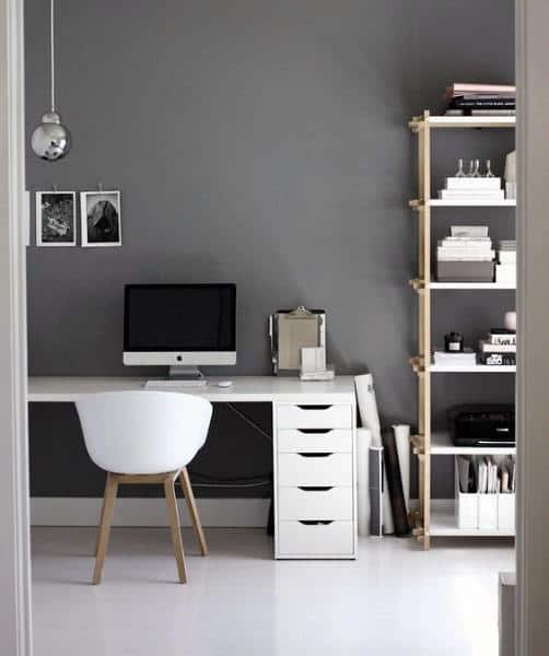 Minimalist home office with a desk, computer, white chair, and shelving unit against a gray wall