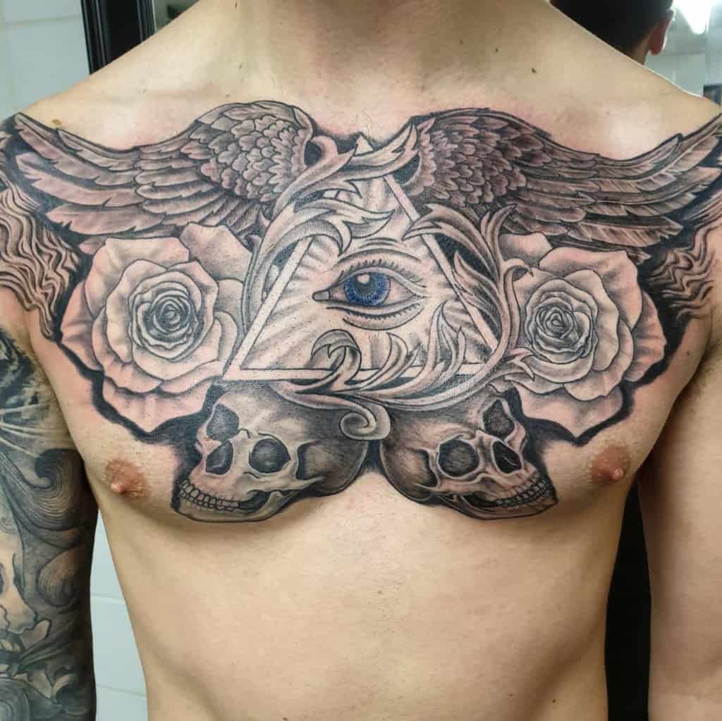 Intricate black and grey chest tattoo featuring an all-seeing eye within a triangle, wings, roses, and skulls, blending symbolism and realism.