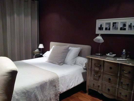 Cozy bedroom with a double bed, red nightstands, and framed pictures on a purple wall, softly lit by lamps