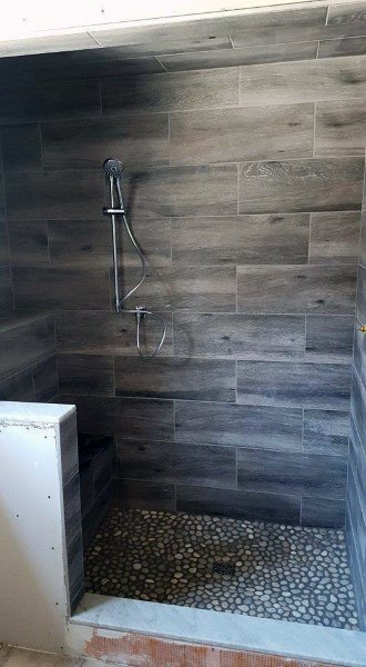 Wood-look travertine tile shower with pebble floor and sleek handheld showerhead.