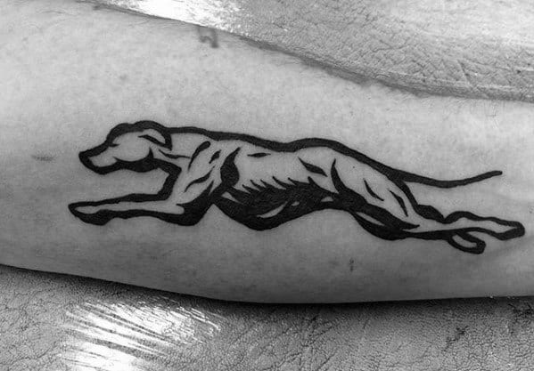 A bold black ink tattoo of a greyhound in full sprint, highlighting the sleek and muscular silhouette of the dog in motion.