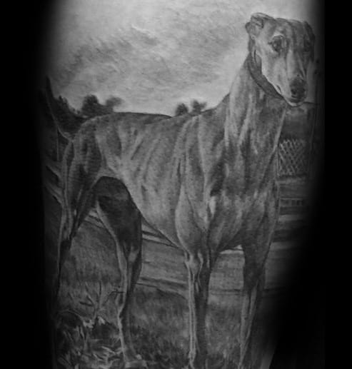A detailed black and grey tattoo of a standing greyhound, capturing the dog's elegant posture and realistic features against a shaded background.
