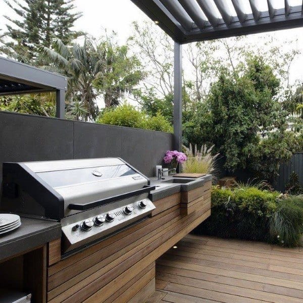 Outdoor kitchen with a gas grill, wooden countertops, and lush greenery in the outdoor backdrop
