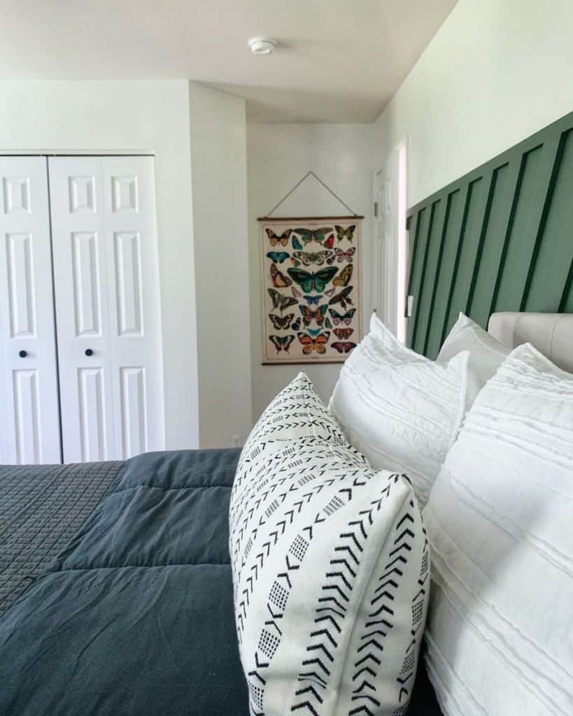 Bright guest bedroom with patterned pillows, dark green accent headboard, and butterfly wall art.