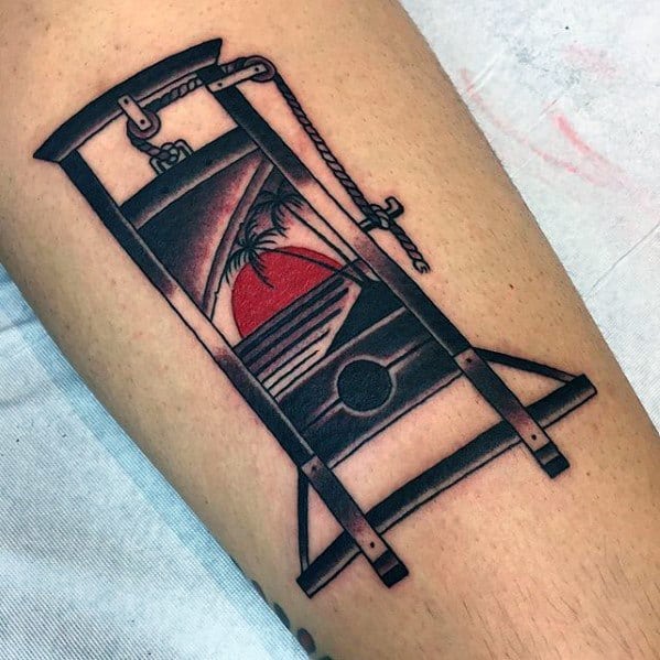 Colorful guillotine tattoo featuring a sunset, palm tree, and ocean view framed within the blade for a surreal tropical twist.