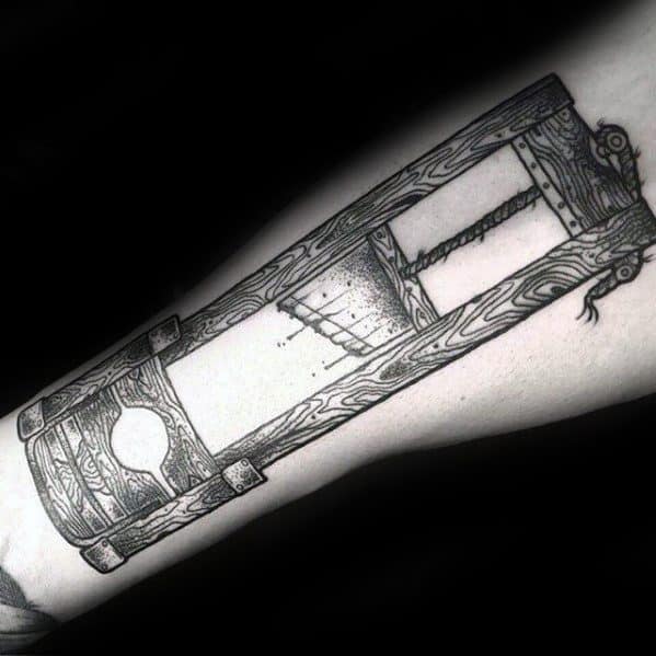 Intricate black and grey guillotine tattoo with detailed wood grain texture, shaded blade, and realistic depth on a clean forearm.