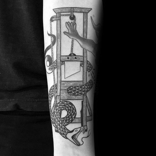 Detailed black and grey guillotine tattoo with a coiled serpent and an outstretched hand reaching toward the falling blade.