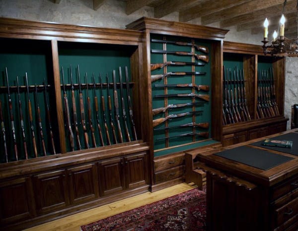 Gun collector's room with wooden cabinets, green backing, and rifles and shotguns on racks.