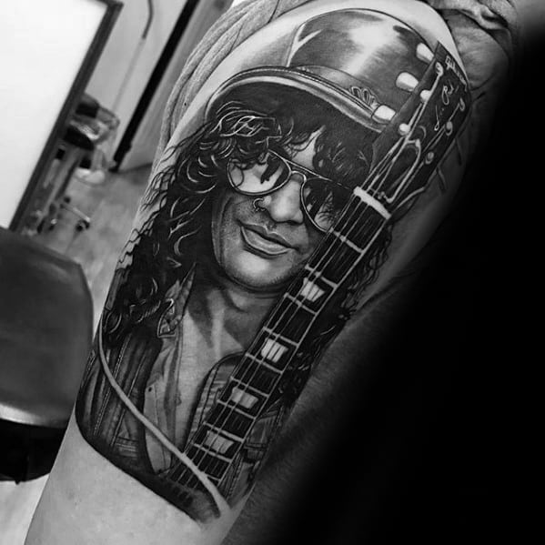 Detailed black and grey tattoo of a smiling guitarist with long curly hair, sunglasses, and a guitar, inspired by Slash of Guns N' Roses.