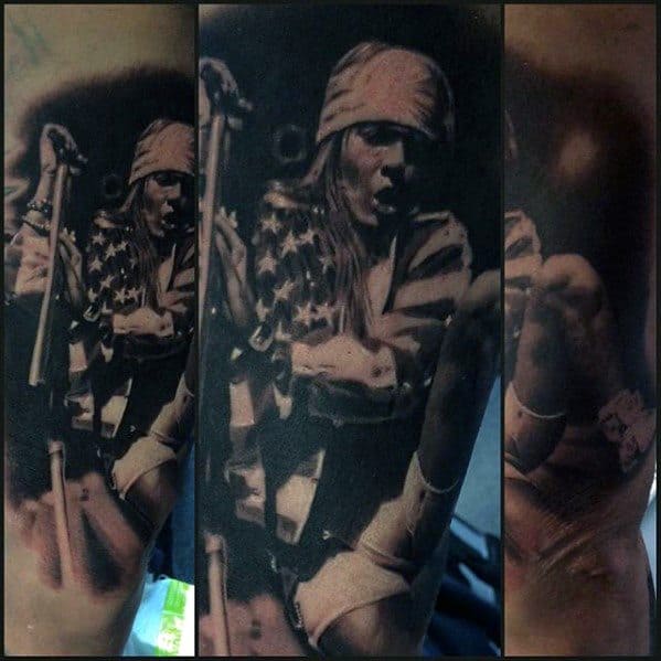 Realistic tattoo of Axl Rose mid-performance, wearing a bandana and American flag jacket, gripping a mic stand in an intense pose.