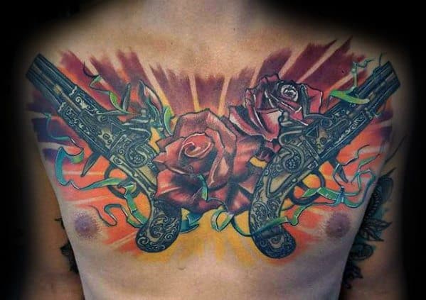 Vibrant chest tattoo of two ornate pistols crossed with red roses and colorful streamers, set against a bold orange and red backdrop.