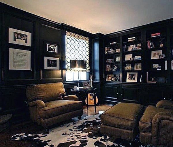 Cozy living room with dark wood paneling, brown armchairs, bookshelf, and a cowhide rug.