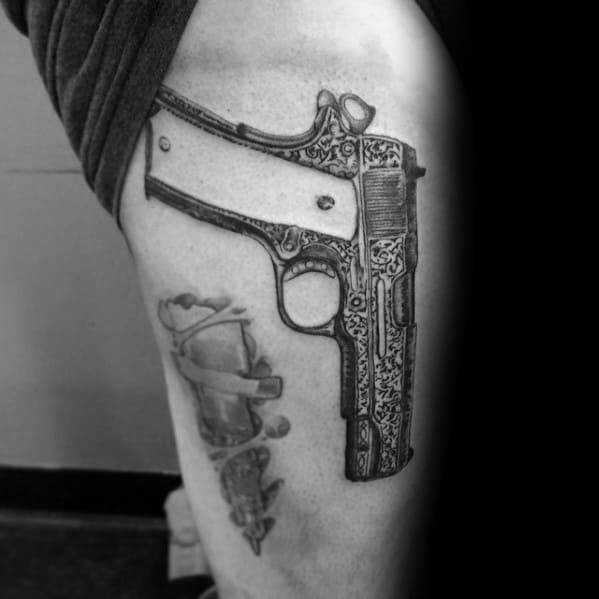 Realistic black and gray tattoo of an engraved 1911 pistol on the thigh, featuring intricate detailing and shading for a bold and artistic look.