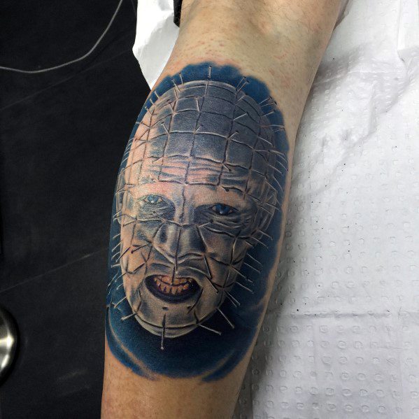 Realistic *Hellraiser* tattoo of Pinhead with a blue-toned background, intricate pin details, and haunting facial expression for a chilling effect.