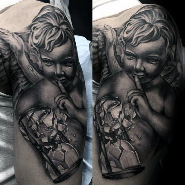 A detailed black and grey tattoo on the upper arm featuring a cherubic angel with a finger to its lips, next to a broken hourglass.