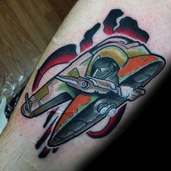 Vibrant tattoo of Boba Fett’s Slave I ship flying over a stylized red and black Mythosaur skull background on the leg.