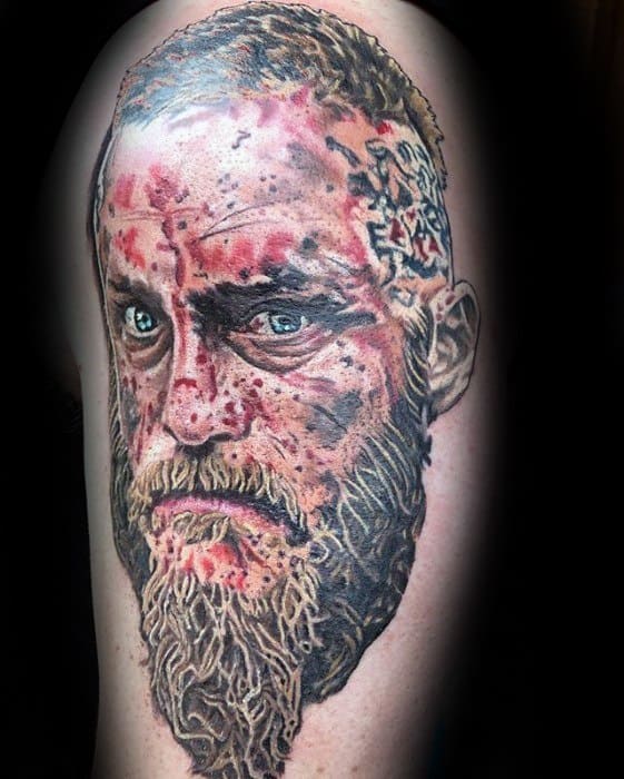 Realistic tattoo of a Ragnar Lothbork's intense face with red, black, and white ink on skin