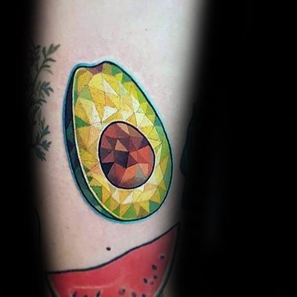 Geometric avocado tattoo with faceted, gem-like shading in yellow, green, and brown tones, creating a unique 3D polygonal effect.