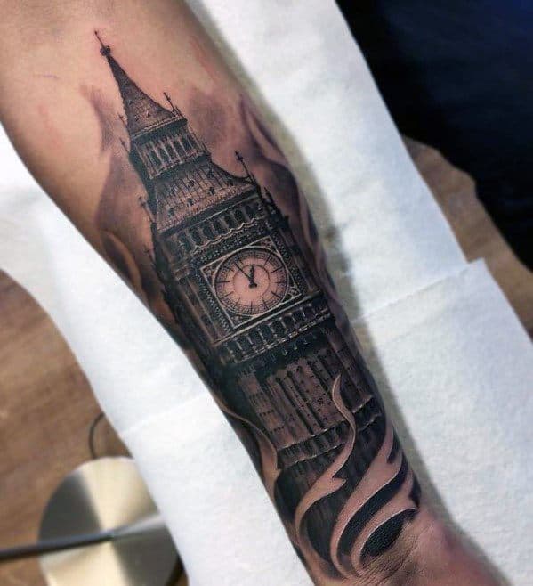 Detailed black and grey tattoo of Big Ben on the forearm, with swirling smoke or flame-like elements around the base, adding dramatic depth and texture.