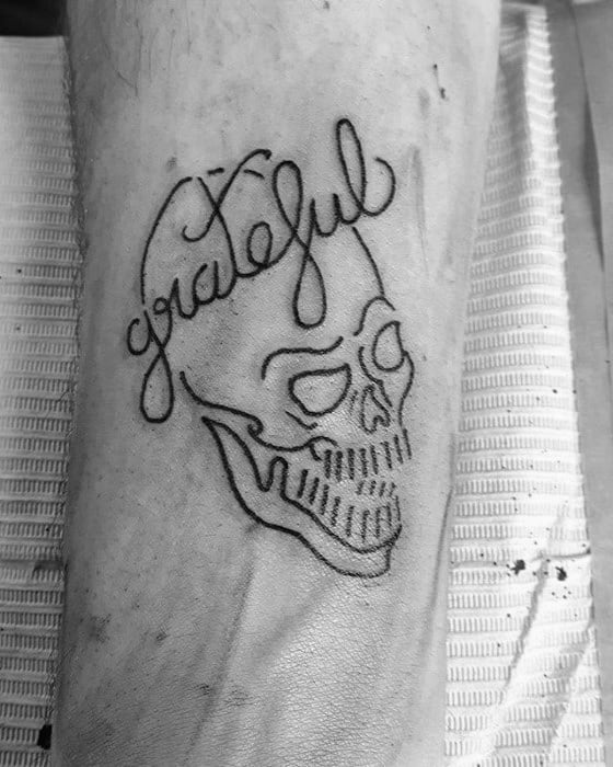 Minimalist Grateful Dead skull tattoo outlined in black with the word “grateful” flowing into the skull’s shape in cursive script.