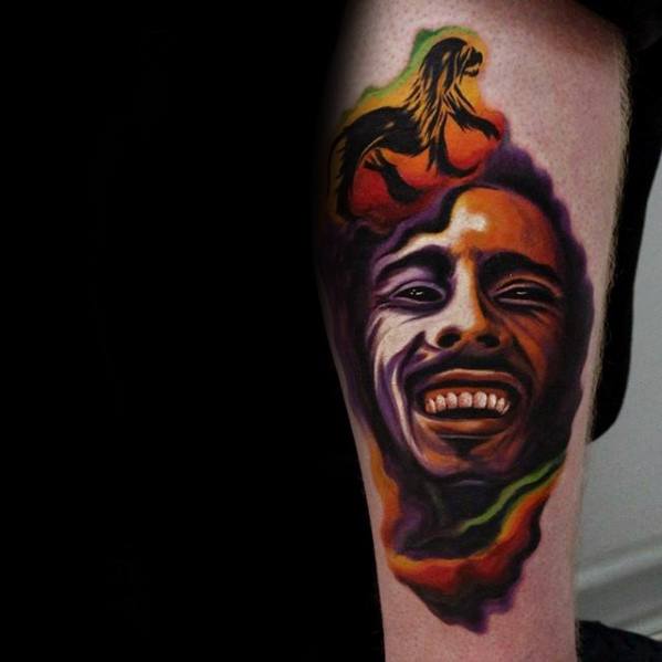 Colorful Bob Marley tattoo with bold red, green, yellow, and purple hues, featuring a smiling portrait and a woman with flowing hair above.