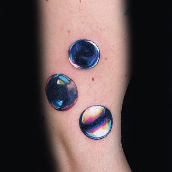 Tattoo of three realistic water droplets with vibrant reflections and highlights, showcasing a glossy and transparent effect for a three-dimensional look.