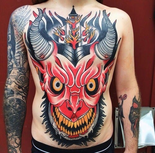Bold chest tattoo of a red demon face with large horns and sharp teeth. A burning church rises between the horns, surrounded by flames.
