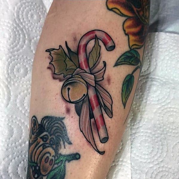 Christmas tattoo of a candy cane tied with a ribbon, featuring holly leaves and a small bell, blending festive holiday charm with a classic design.