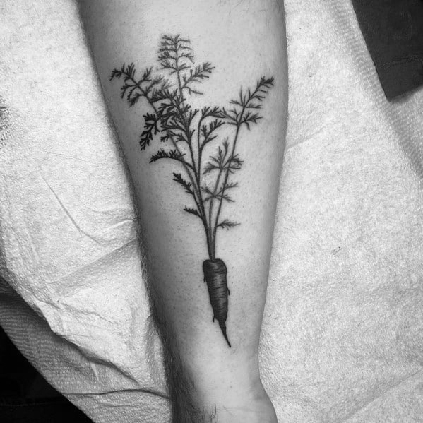 Realistic black ink carrot tattoo on the forearm with fine line detailing and delicate leafy tops for a clean and natural botanical design.