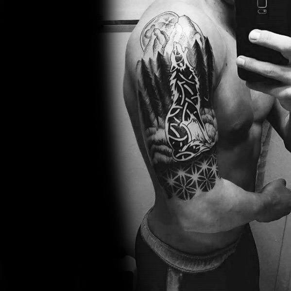 Black and grey upper arm tattoo featuring a howling Celtic wolf with intricate knotwork, surrounded by trees and a moonlit background