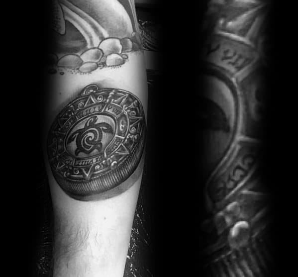 Intricate tattoo of an ornate coin with detailed engravings, featuring bold shading and a three-dimensional effect on the forearm.