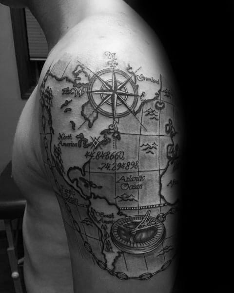 Intricate map-themed coordinate tattoo on the upper arm with a compass, ocean details, and fine linework, symbolizing adventure and exploration.