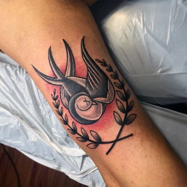 Tattoo of a stylized sparrow bird and laurel wreath on the inside of an arm