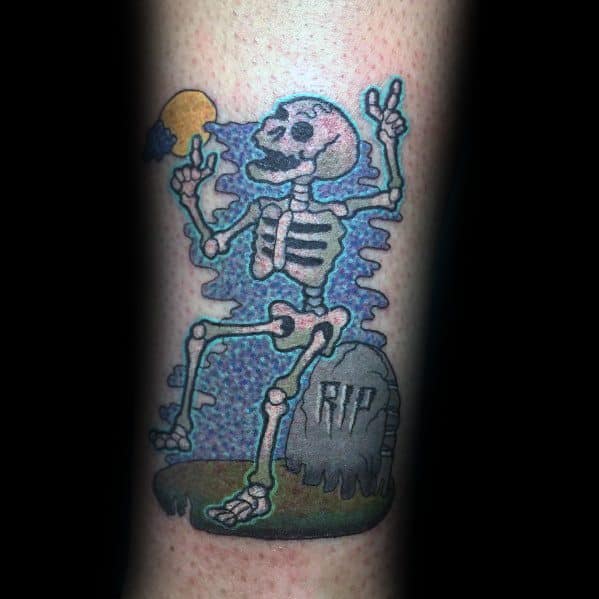 Playful skeleton tattoo sitting on a tombstone with "RIP," flashing peace signs, and a colorful night sky, creating a fun and spooky vibe.