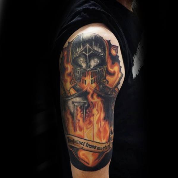Dark Souls-inspired upper arm tattoo of a knight's helmet engulfed in flames, with crossed swords and a Latin banner reading “Vindicisci trans mortem.”