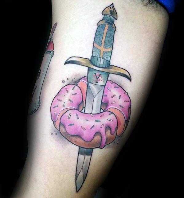Tattoo of a dagger piercing through a pink frosted donut with sprinkles, combining sweet and edgy elements in a bold design.