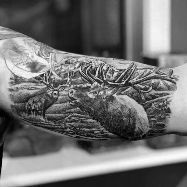 Realistic black and grey elk tattoo on the forearm, featuring detailed shading, a rugged landscape, and multiple elk for a bold nature-inspired design.