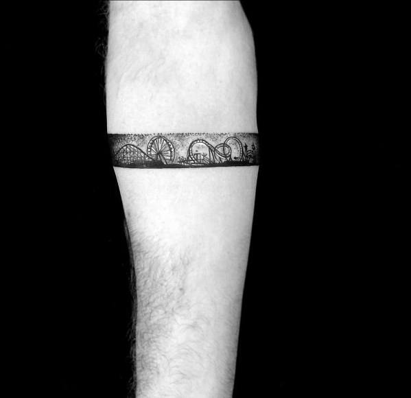 Amusement park armband tattoo featuring a Ferris wheel, roller coaster, and city skyline in fine detail, creating a sleek and dynamic design.