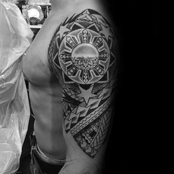 Filipino sun tattoo on the upper arm with detailed tribal rays, central shading, large stars, and woven patterns forming a full half-sleeve.