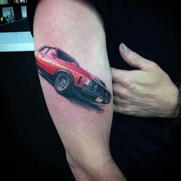 Colorful Ford muscle car tattoo on upper arm, featuring a bold red and black design with realistic shading and a dynamic perspective.