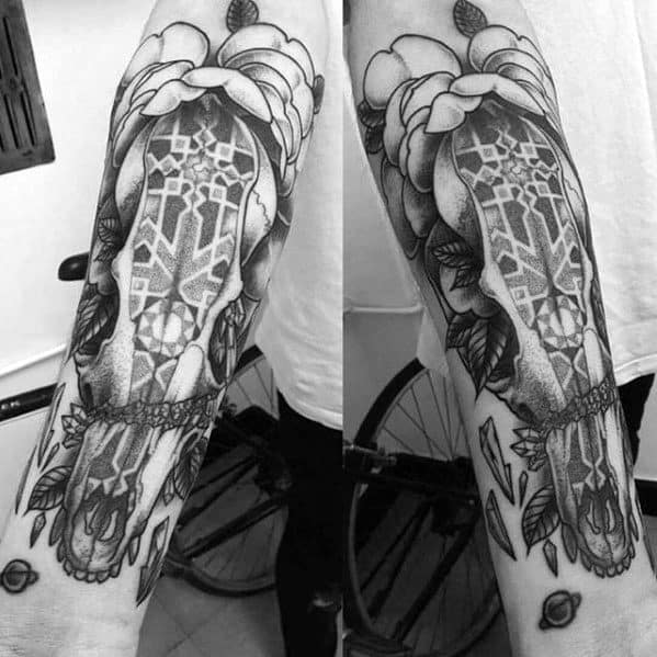 Blackwork tattoo of a fox skull with geometric pattern on top, framed by large flowers and leaves on the forearm.