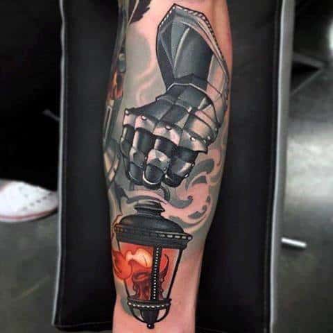 Realistic tattoo of a dark armored gauntlet with smoke-like shading, paired with a glowing lantern containing a red and orange flame.