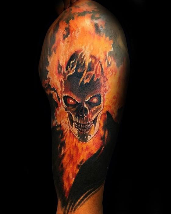 Ghost Rider upper arm tattoo with a fiery skull, glowing red eyes, and intense flames rising in vivid orange and yellow tones.